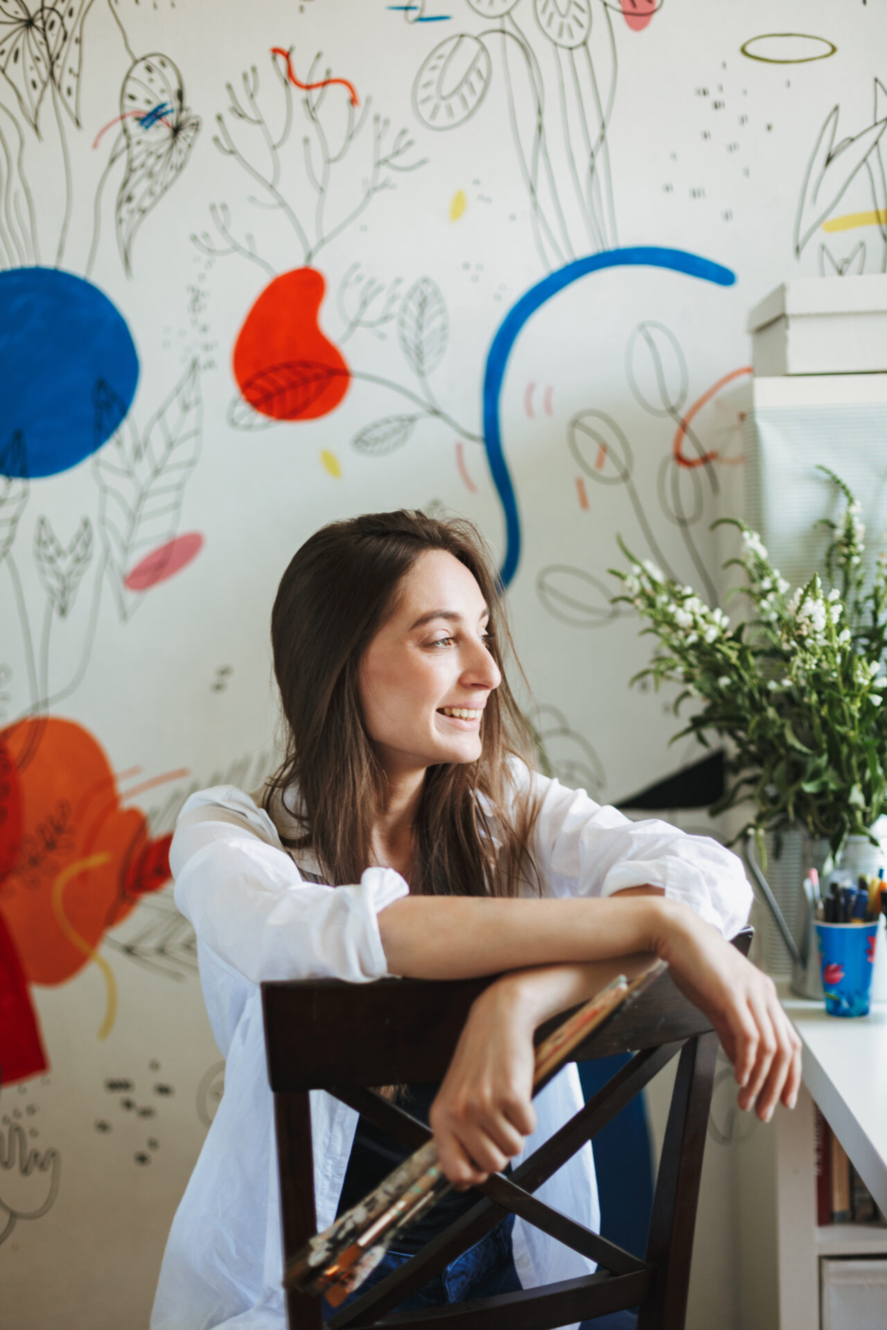 Young smiling painter in white shirt on chair joyfully looking a